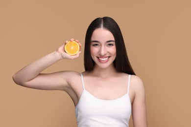 Photo of Beautiful young woman with piece of orange on beige background