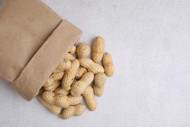 Paper bag with fresh unpeeled peanuts on grey table, top view. Space for text