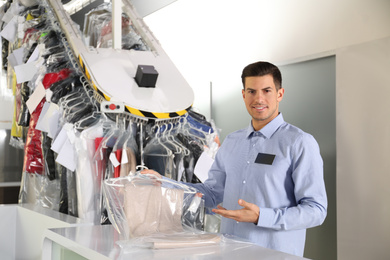 Portrait of happy worker with clothes near counter at dry-cleaner's