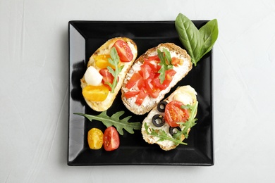 Photo of Plate of delicious tomato bruschettas on light grey background, top view