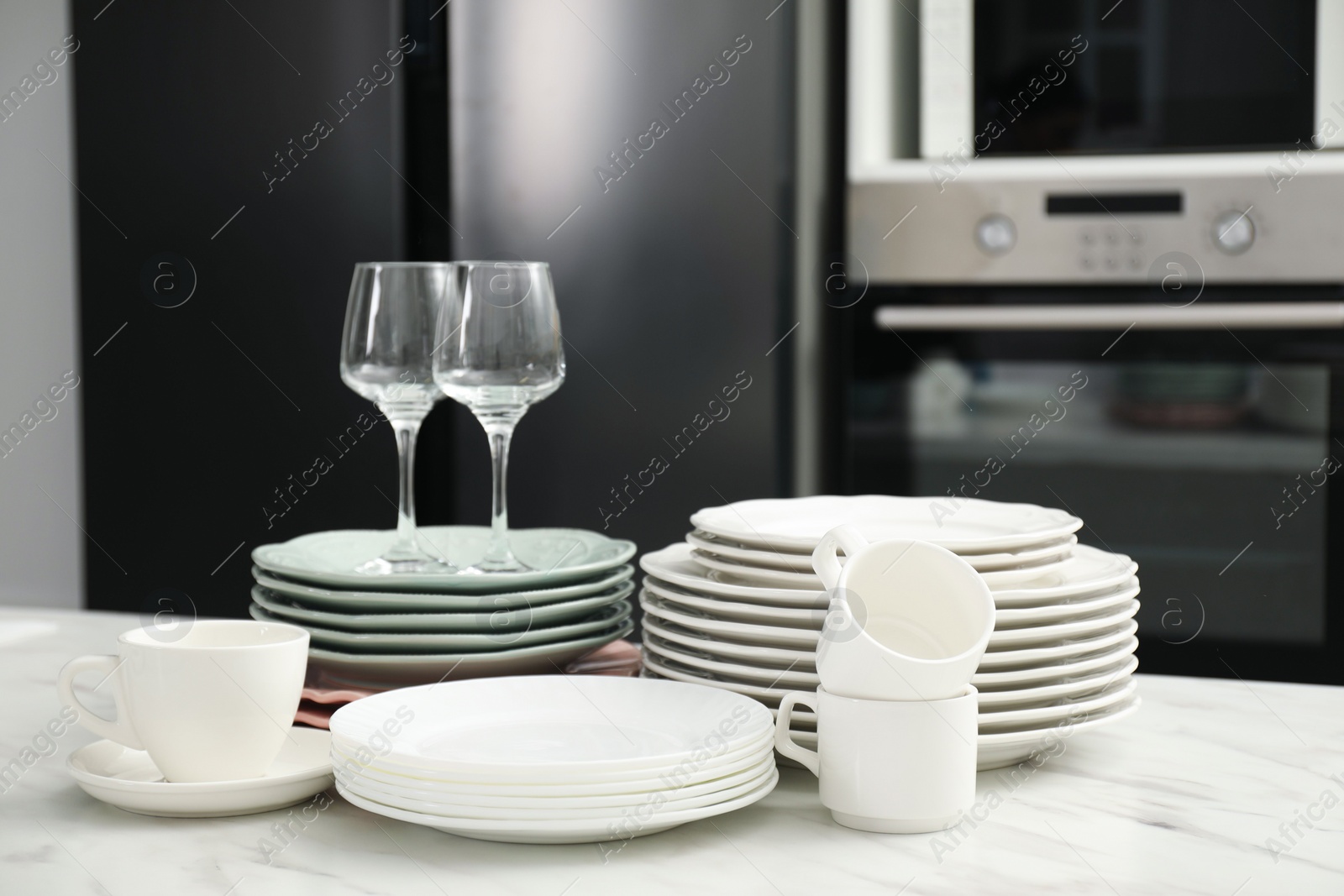 Photo of Clean plates, cups and glasses on white marble table in kitchen