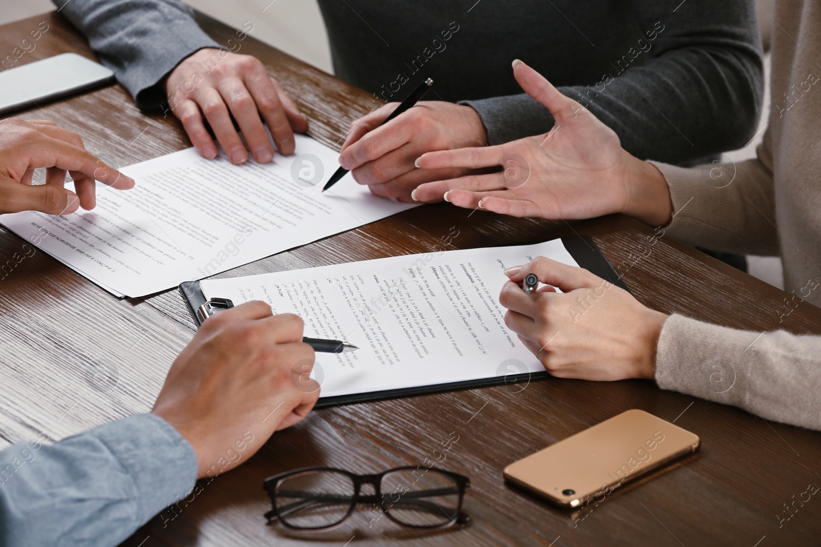 Photo of Notary helping couple with paperwork at wooden table, closeup