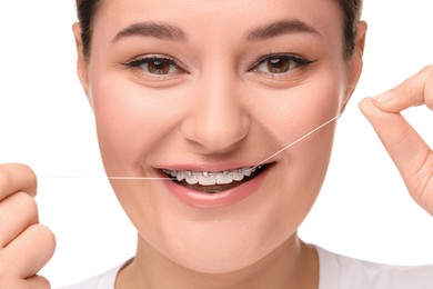 Smiling woman with braces cleaning teeth using dental floss on white background, closeup