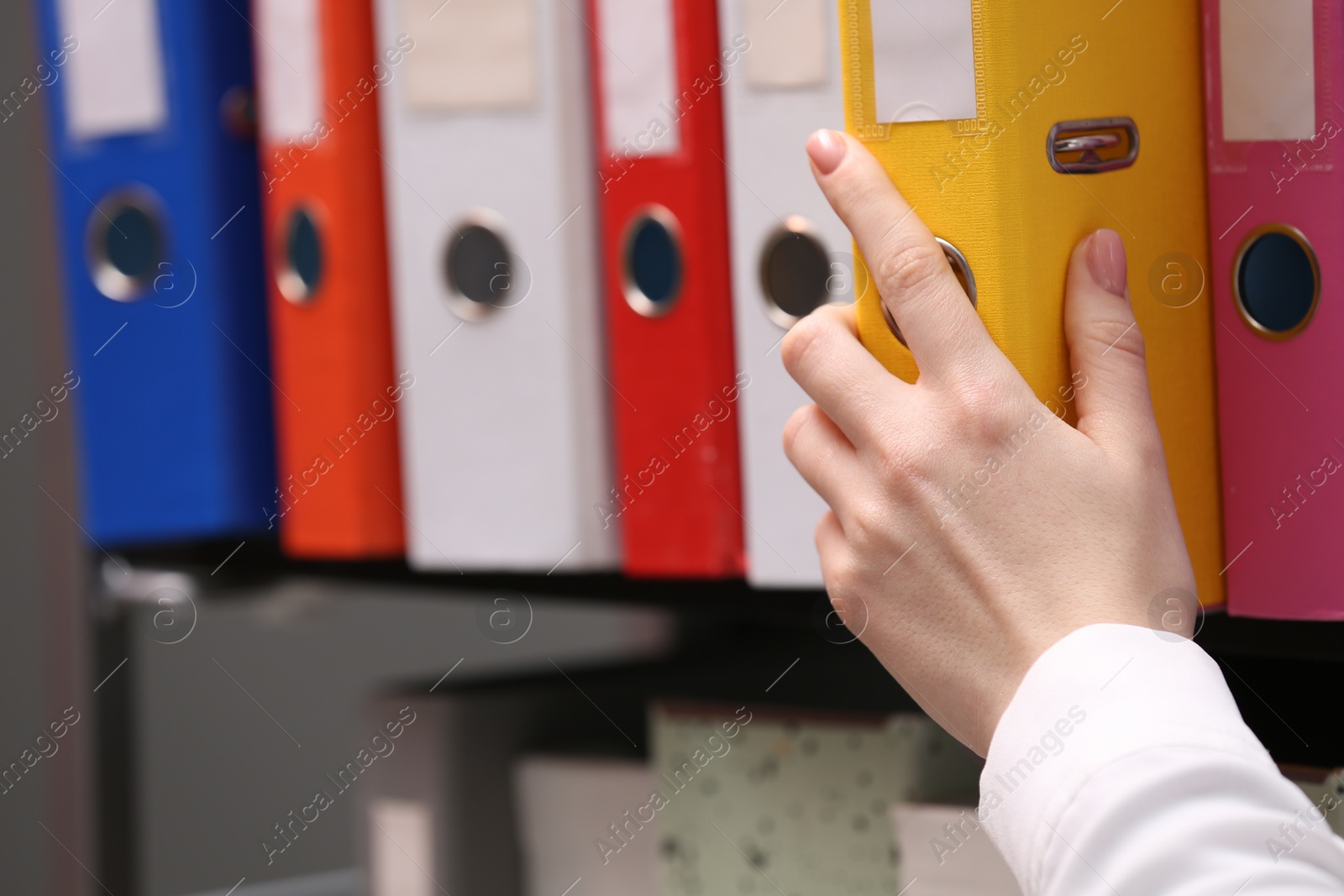 Photo of Woman taking folder with documents from shelf in office, closeup