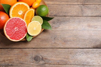 Photo of Fresh juicy citrus fruits with green leaves on wooden table, top view. Space for text