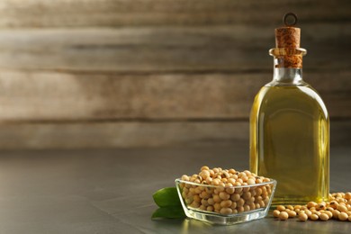 Photo of Glass bottle of oil, leaves and soybeans on grey table. Space for text