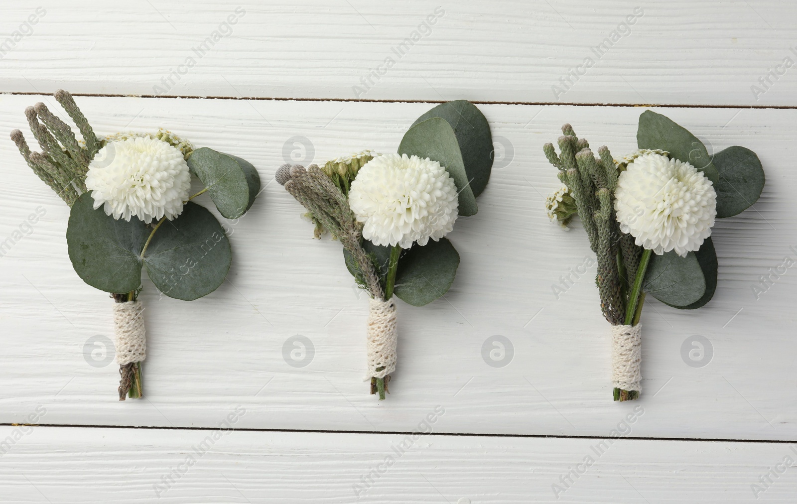 Photo of Small stylish boutonnieres on white wooden table, flat lay