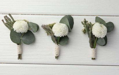 Small stylish boutonnieres on white wooden table, flat lay