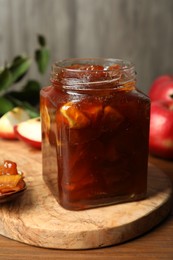 Photo of Tasty apple jam in glass jar on wooden table, closeup
