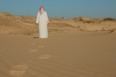 Photo of Man in arabic clothes walking through desert on sunny day, back view