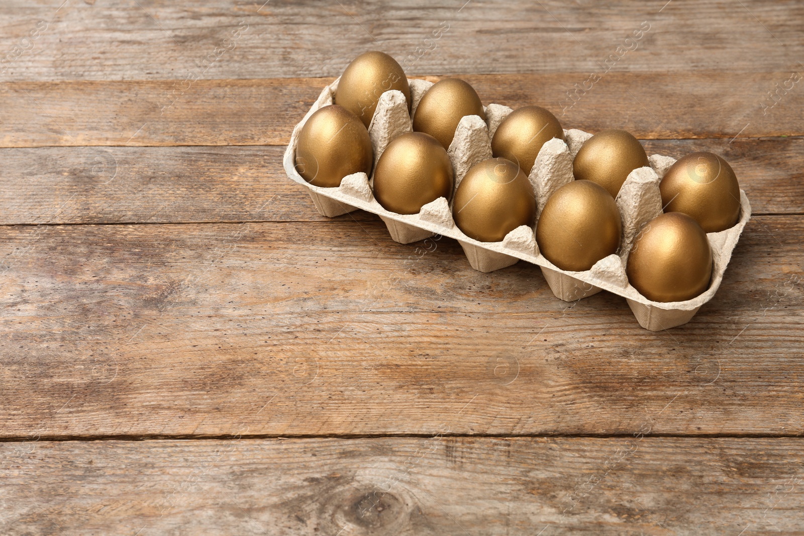 Photo of Carton with golden eggs on wooden table, space for text