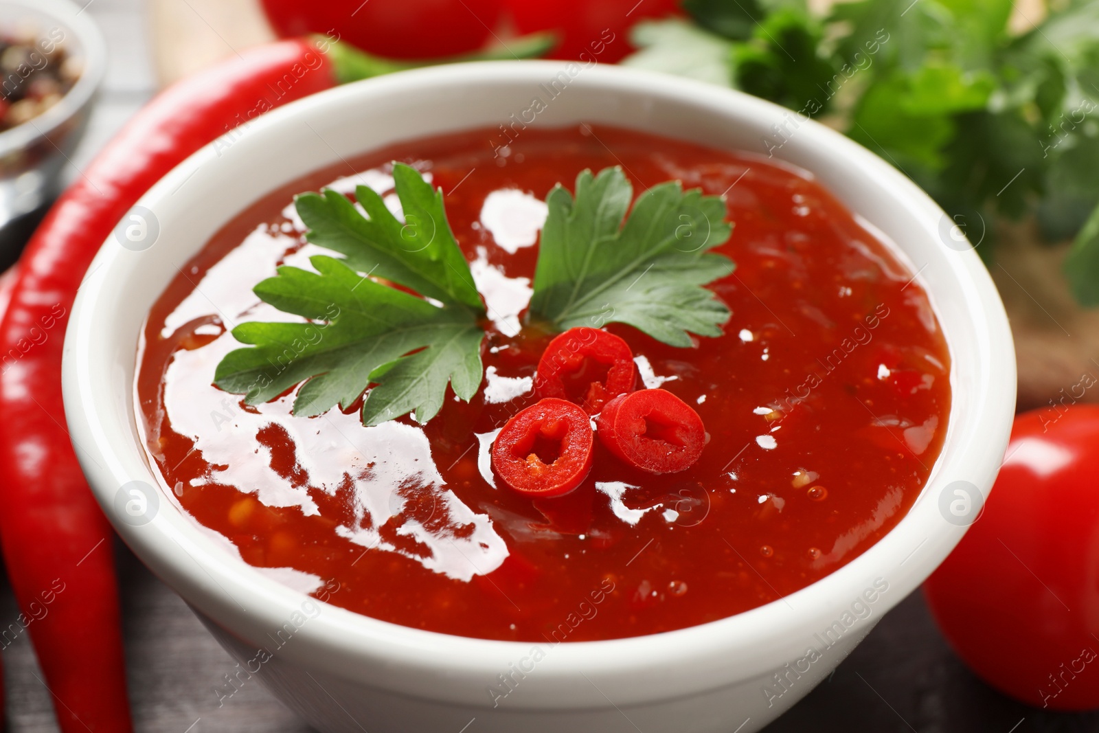 Photo of Spicy chili sauce with parsley on table, closeup