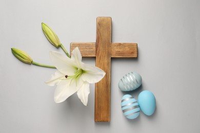 Wooden cross, painted Easter eggs and lily flowers on grey background, flat lay