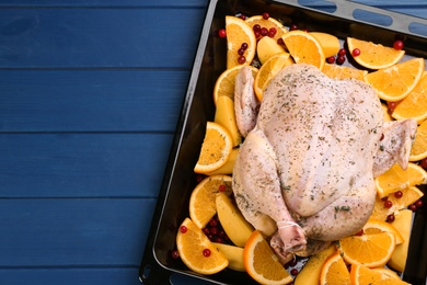 Raw chicken with orange slices, potatoes and cranberries on blue wooden table, top view. Space for text