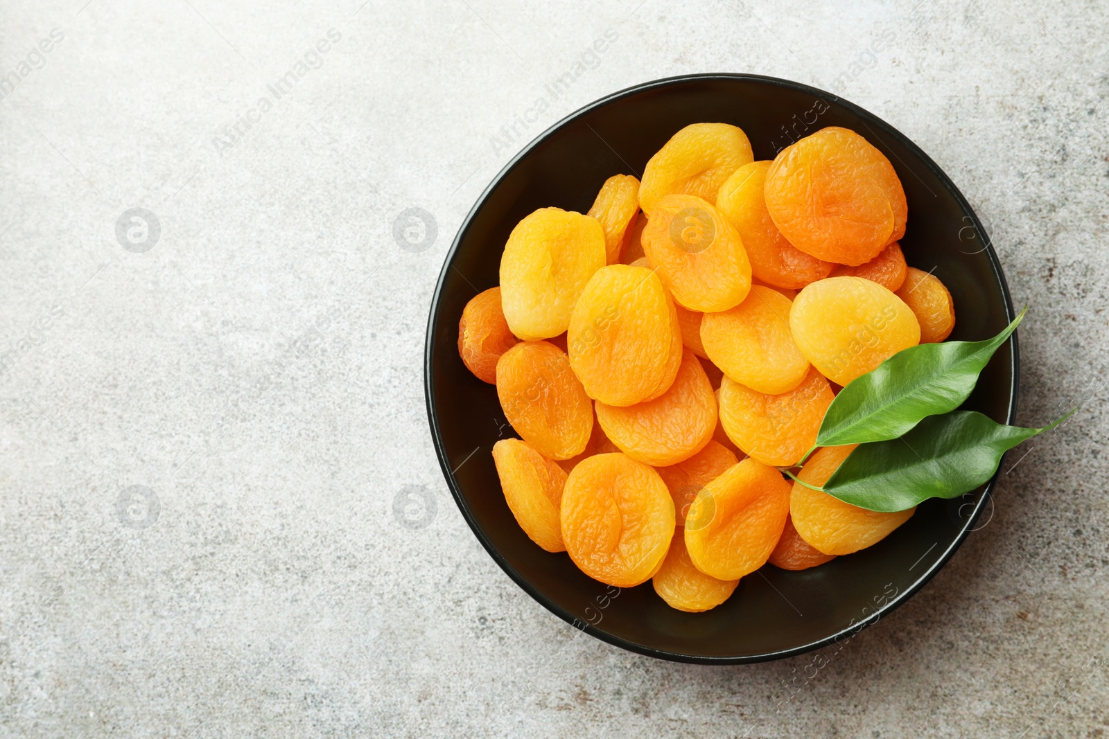 Photo of Plate of tasty apricots and space for text on grey table, top view. Dried fruits