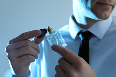 Photo of Handsome man applying perfume on neck against light background, closeup. Blue filter effect