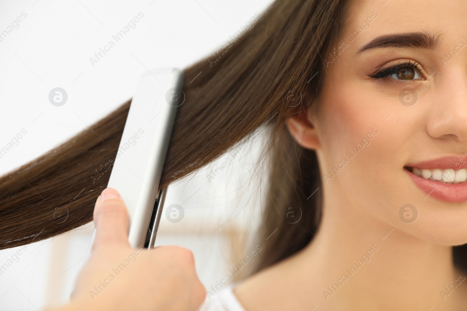 Photo of Hairdresser using modern flat iron to style client's hair in salon, closeup