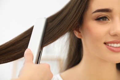 Photo of Hairdresser using modern flat iron to style client's hair in salon, closeup