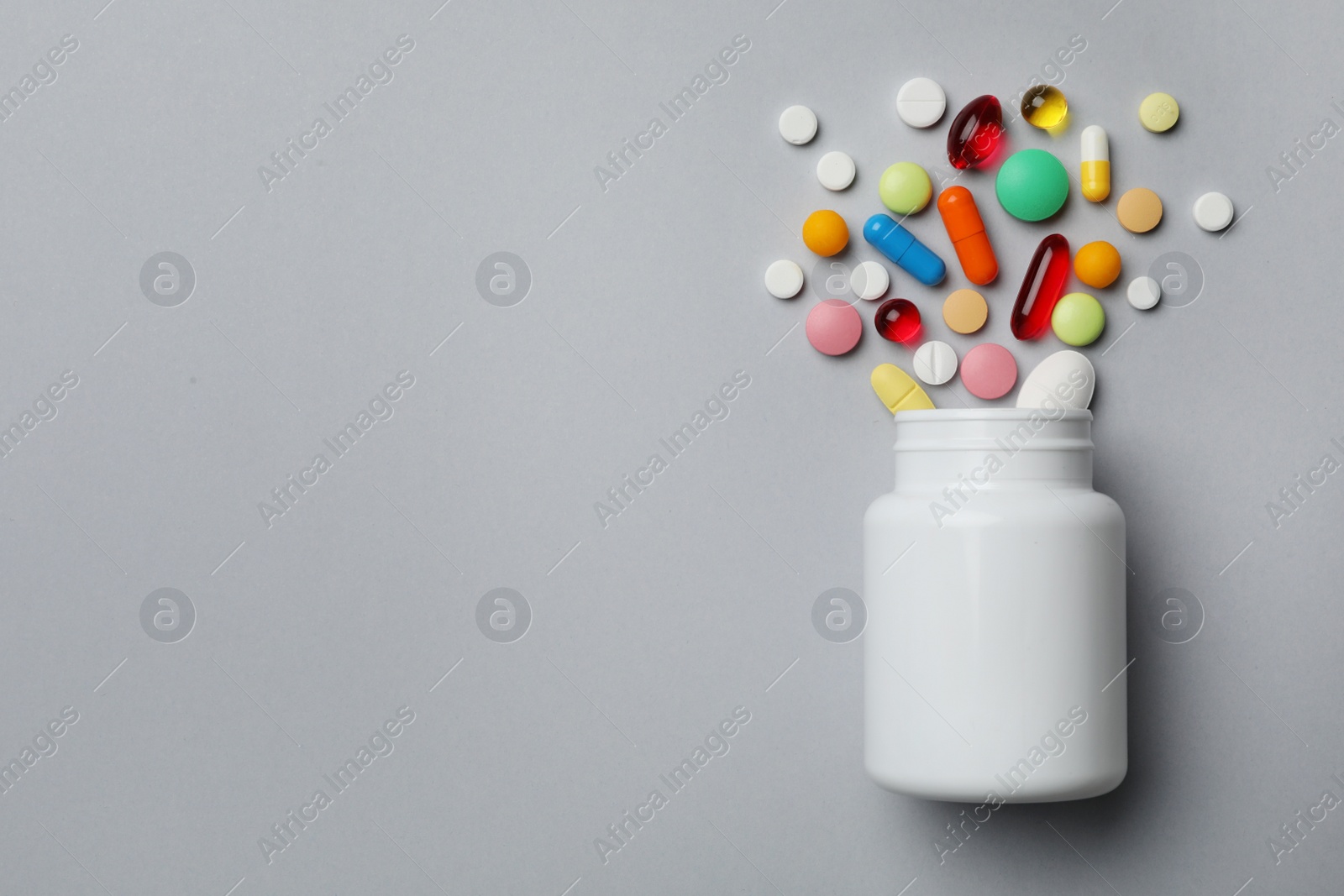 Photo of Bottle with different pills on grey background, flat lay. Space for text