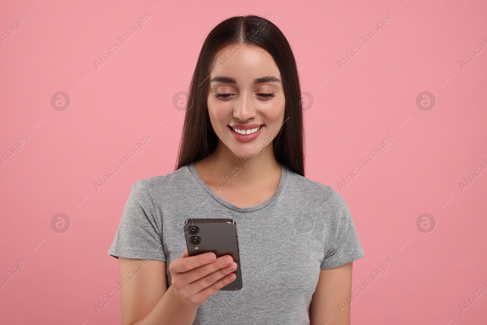 Photo of Happy young woman looking at smartphone on pink background