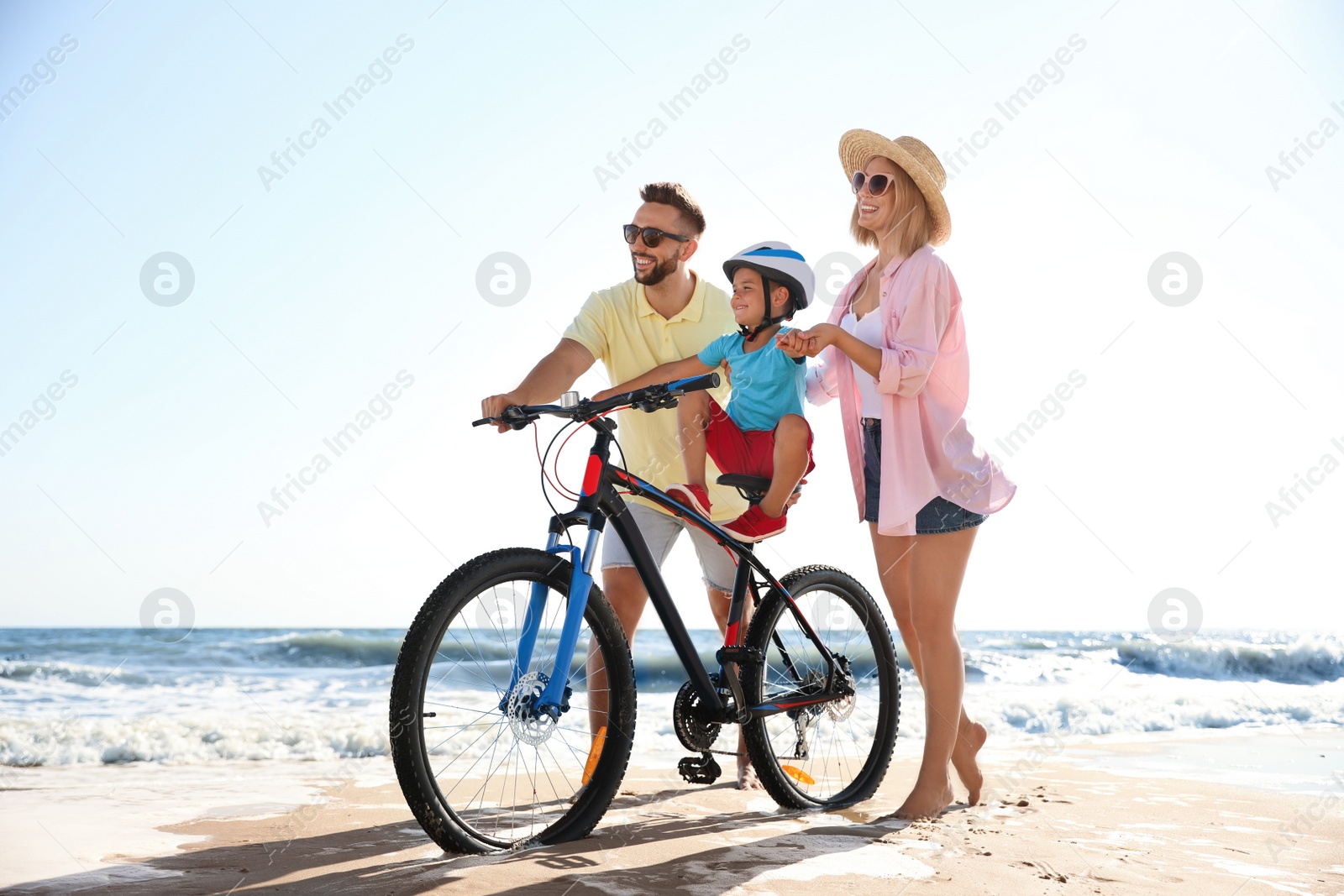 Photo of Happy parents teaching son to ride bicycle on sandy beach near sea