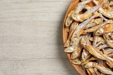 Plate of tasty dried anchovies on light wooden table, top view. Space for text