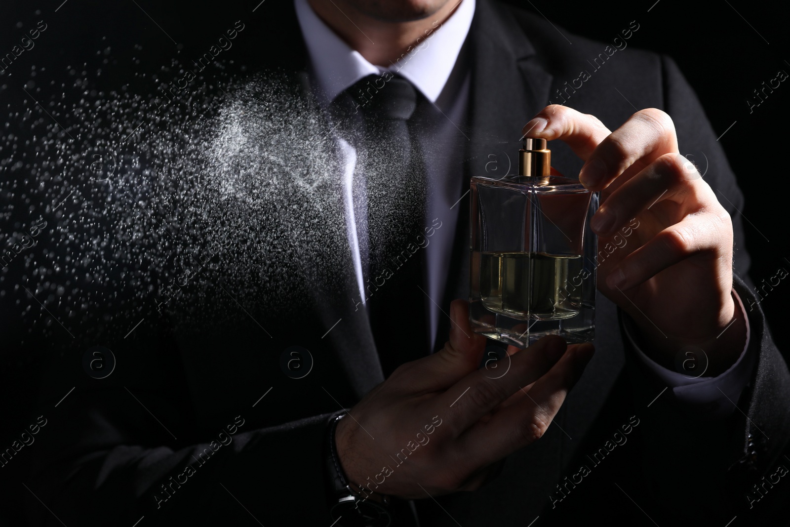 Photo of Man spraying luxury perfume on black background, closeup