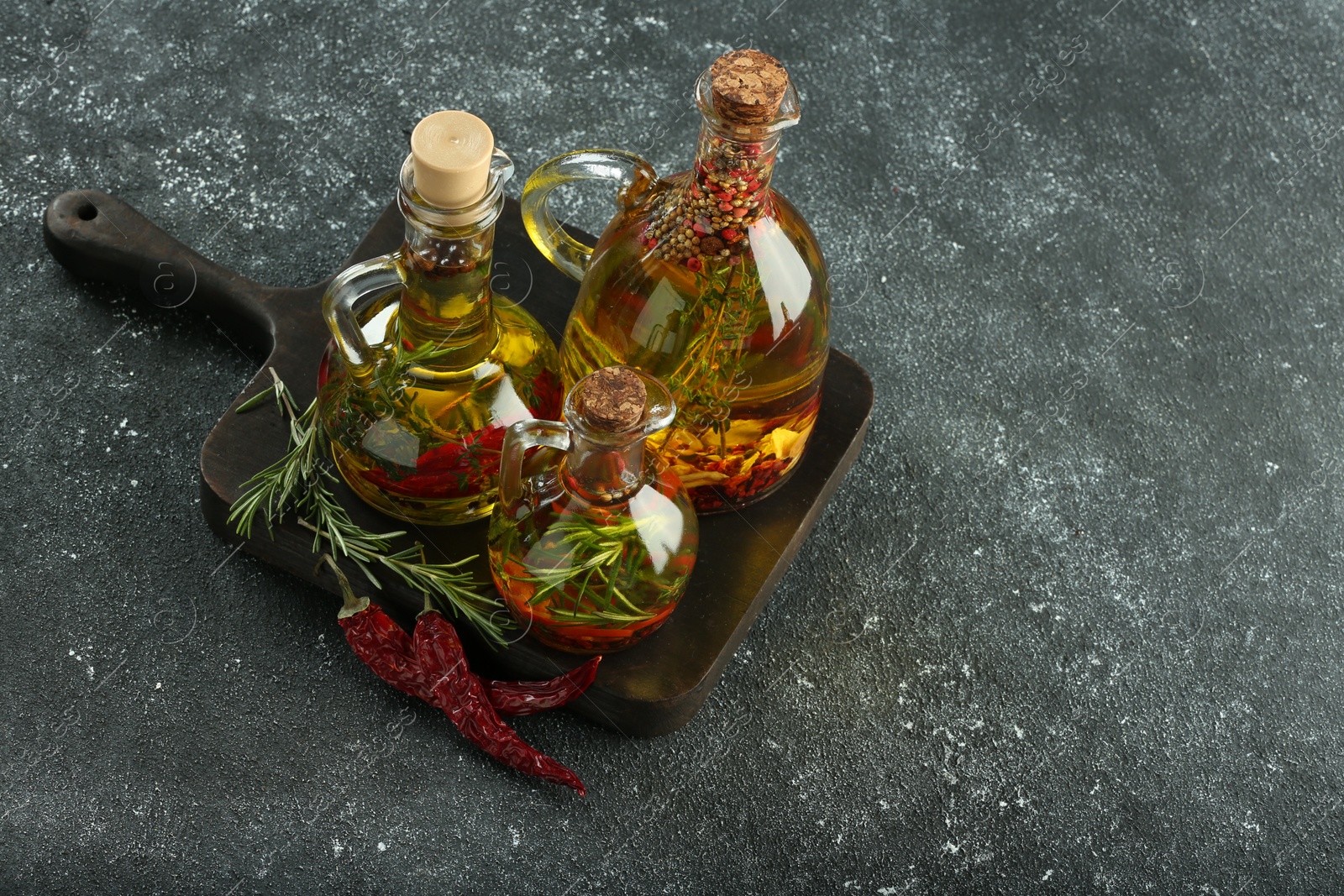 Photo of Cooking oil with different spices and herbs in jugs on light grey table, above view. Space for text