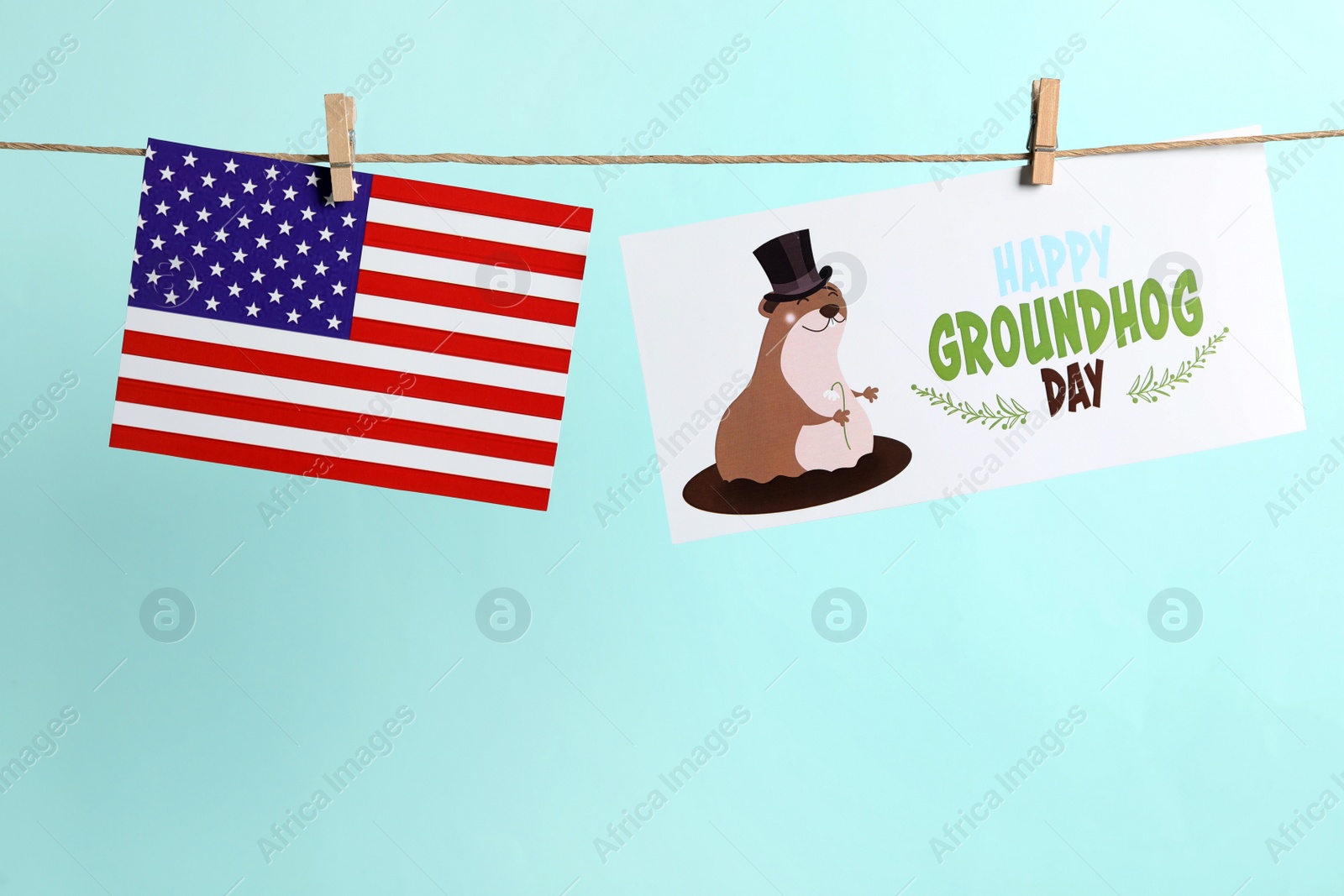 Photo of Happy Groundhog Day greeting card and American flag hanging on turquoise background, space for text