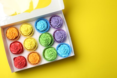 Photo of Tasty cupcakes in box on yellow background, top view. Space for text