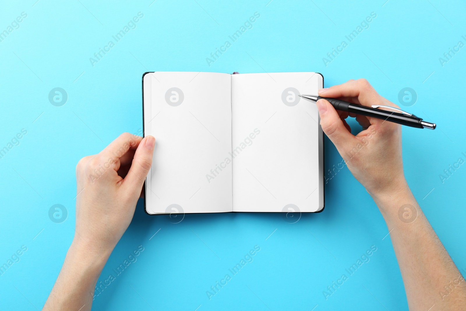 Photo of Woman writing in notebook on light blue background, top view