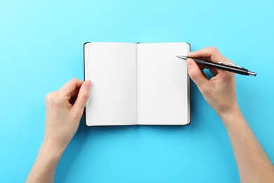 Woman writing in notebook on light blue background, top view