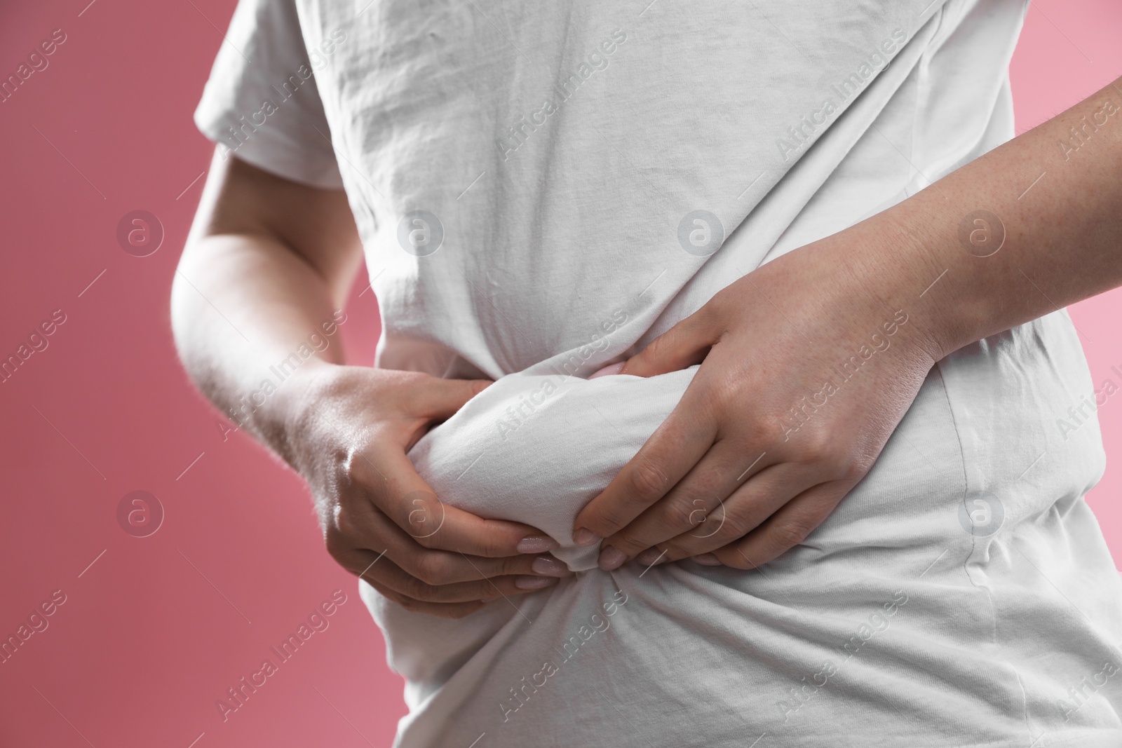 Photo of Woman touching belly fat on pink background, closeup. Overweight problem