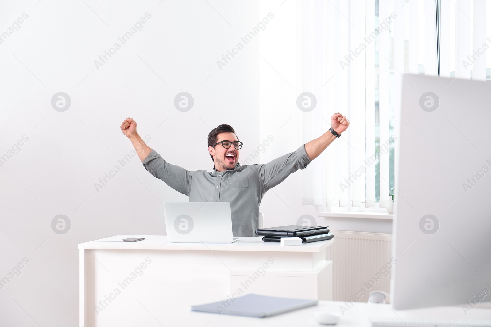 Photo of Excited young man working with laptop at table in office