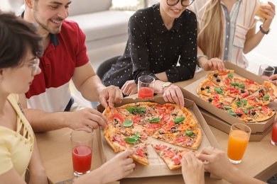 Photo of Young people eating delicious pizzas at table, closeup