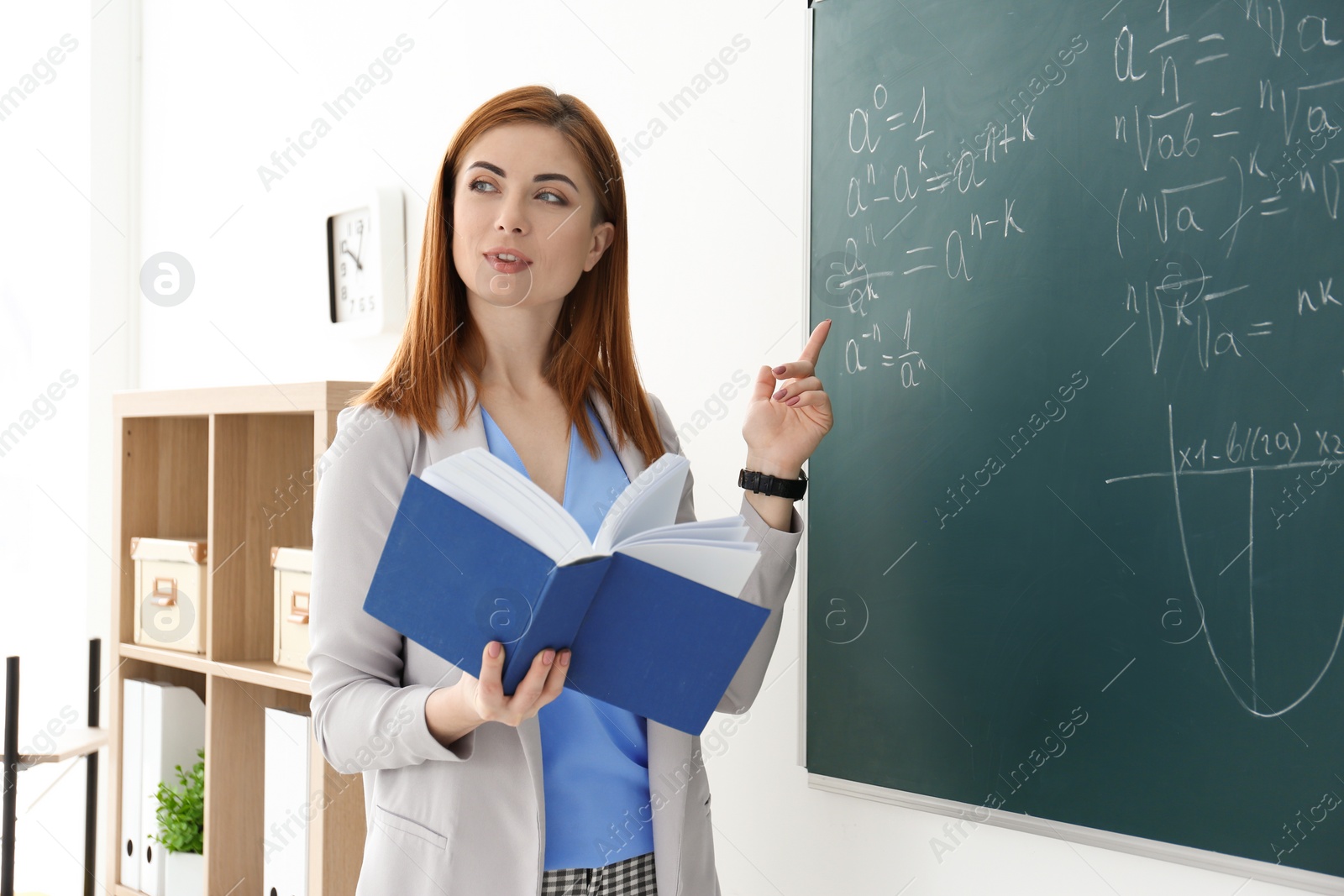 Photo of Beautiful young teacher explaining math formulas written on blackboard in classroom