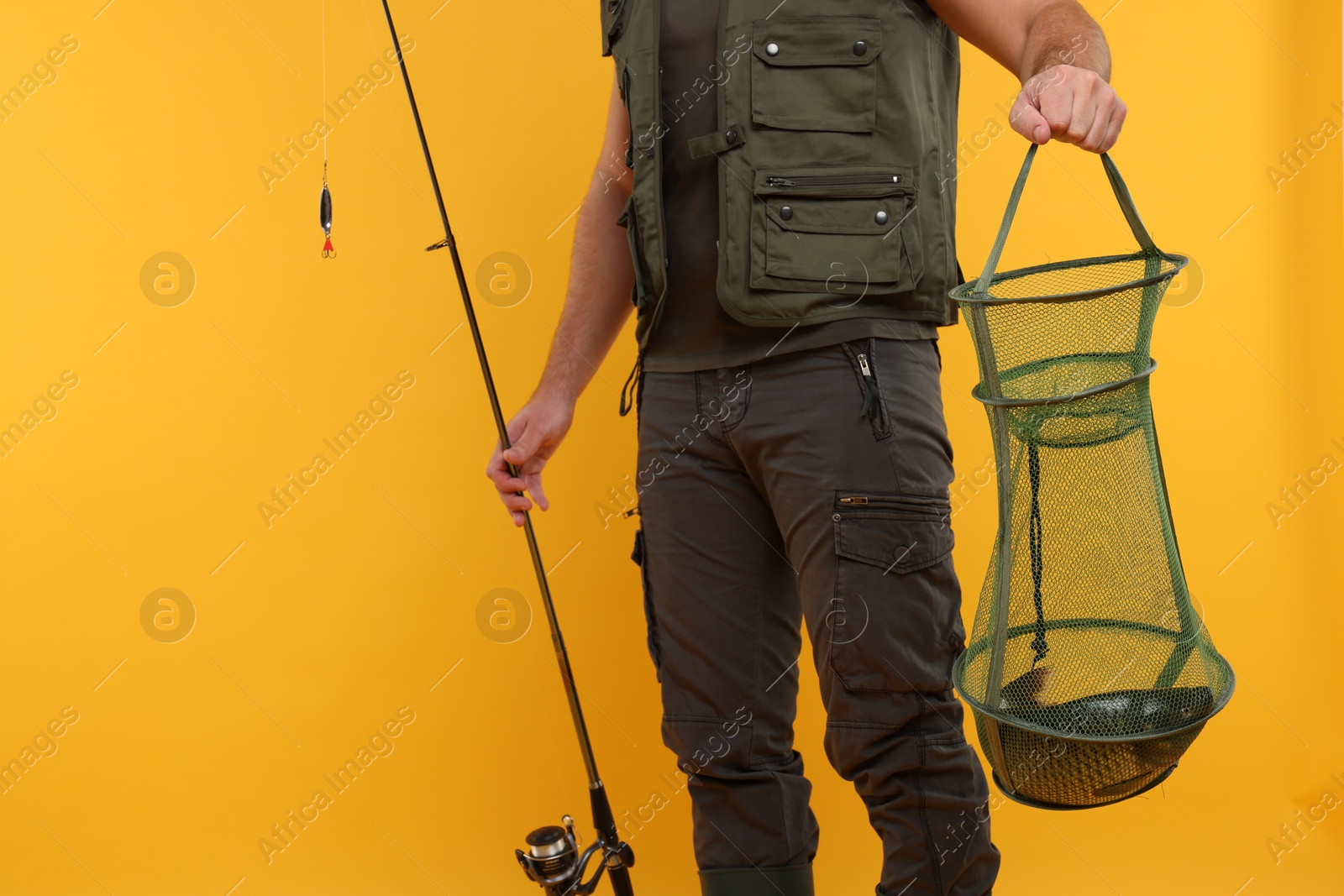 Photo of Fisherman holding rod and fishing net with catch on yellow background, closeup