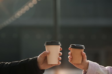 Photo of Man and woman holding paper coffee cups outdoors, closeup