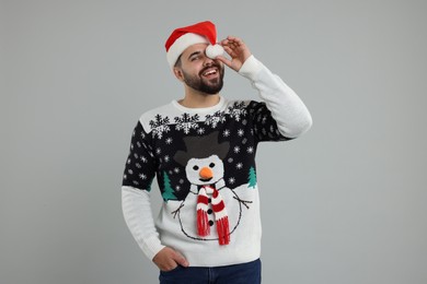 Photo of Happy young man in Christmas sweater and Santa hat on grey background