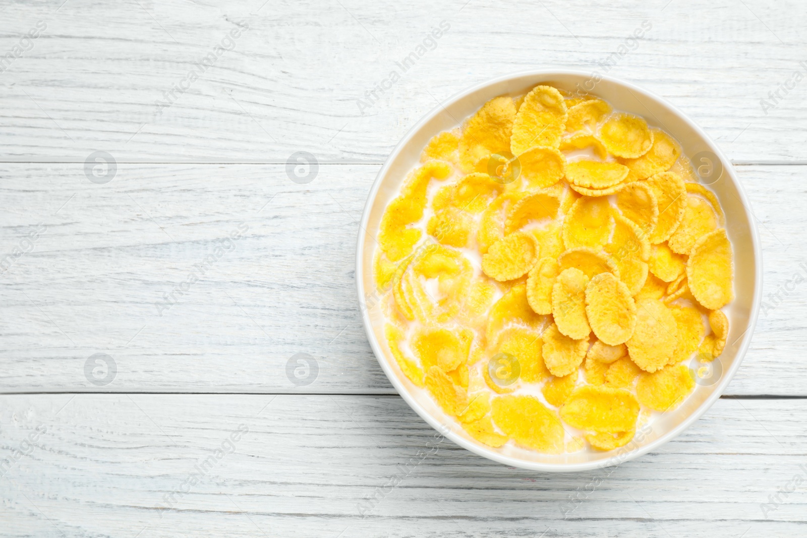 Photo of Tasty corn flakes with milk on white wooden table, top view. Space for text