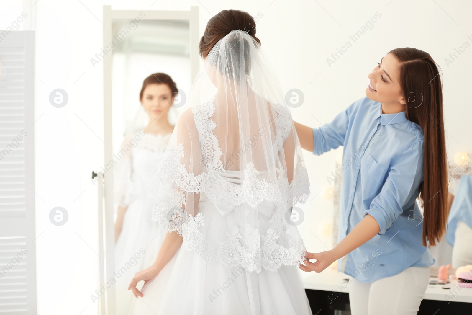 Photo of Fashion stylist preparing bride before her wedding in room