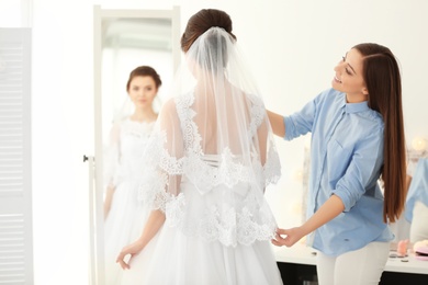 Photo of Fashion stylist preparing bride before her wedding in room