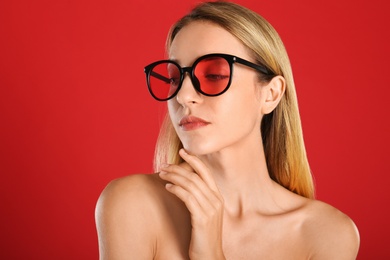 Photo of Beautiful woman in stylish sunglasses on red background