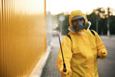 Photo of Person in hazmat suit disinfecting street with sprayer. Surface treatment during coronavirus pandemic