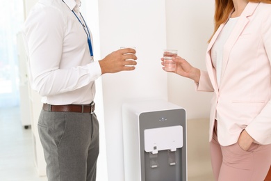 Photo of Co-workers having break near water cooler at workplace, closeup