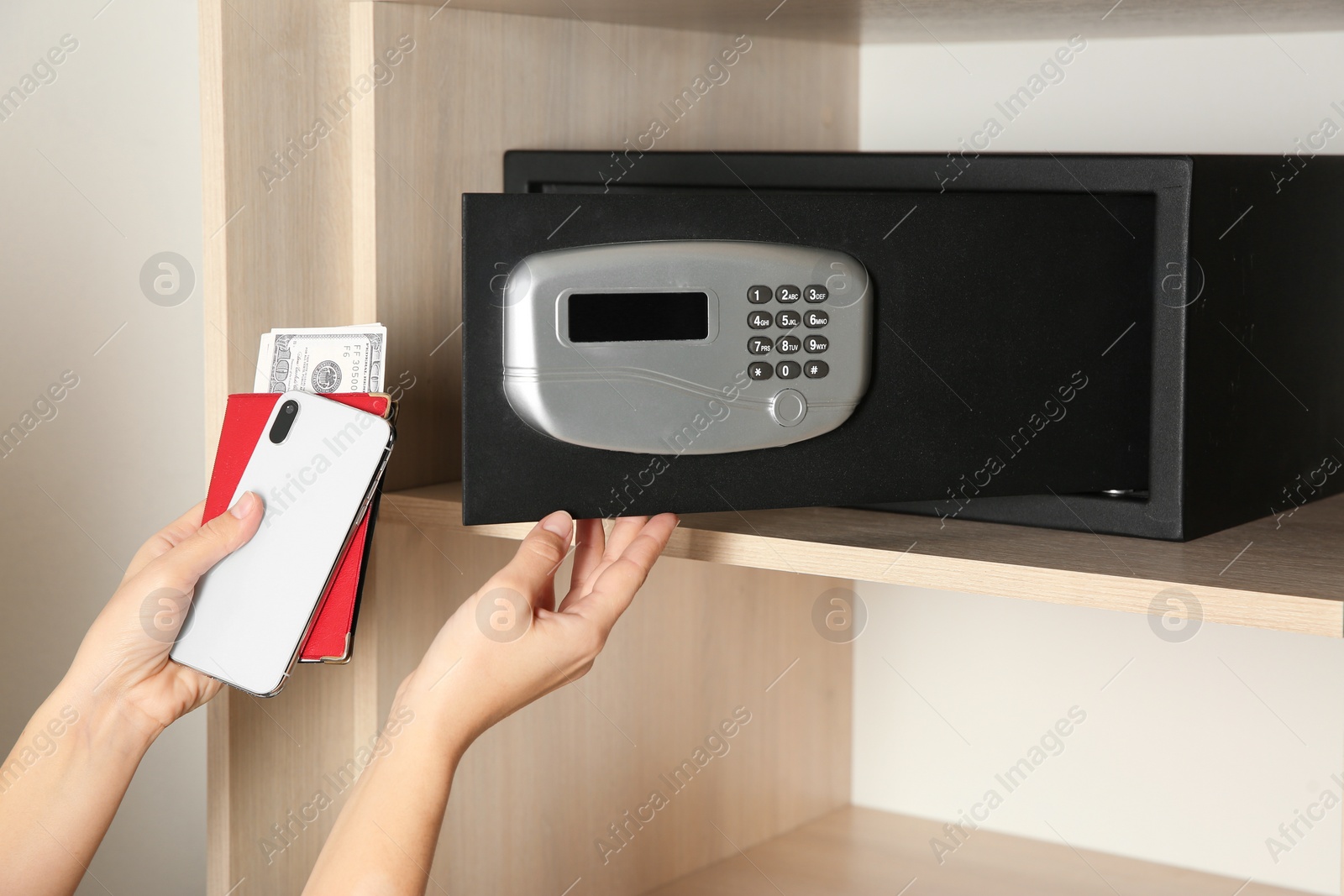 Photo of Woman putting smartphone, passport and money into steel safe, closeup