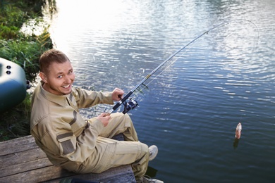 Photo of Man with rod fishing on wooden pier at riverside. Recreational activity