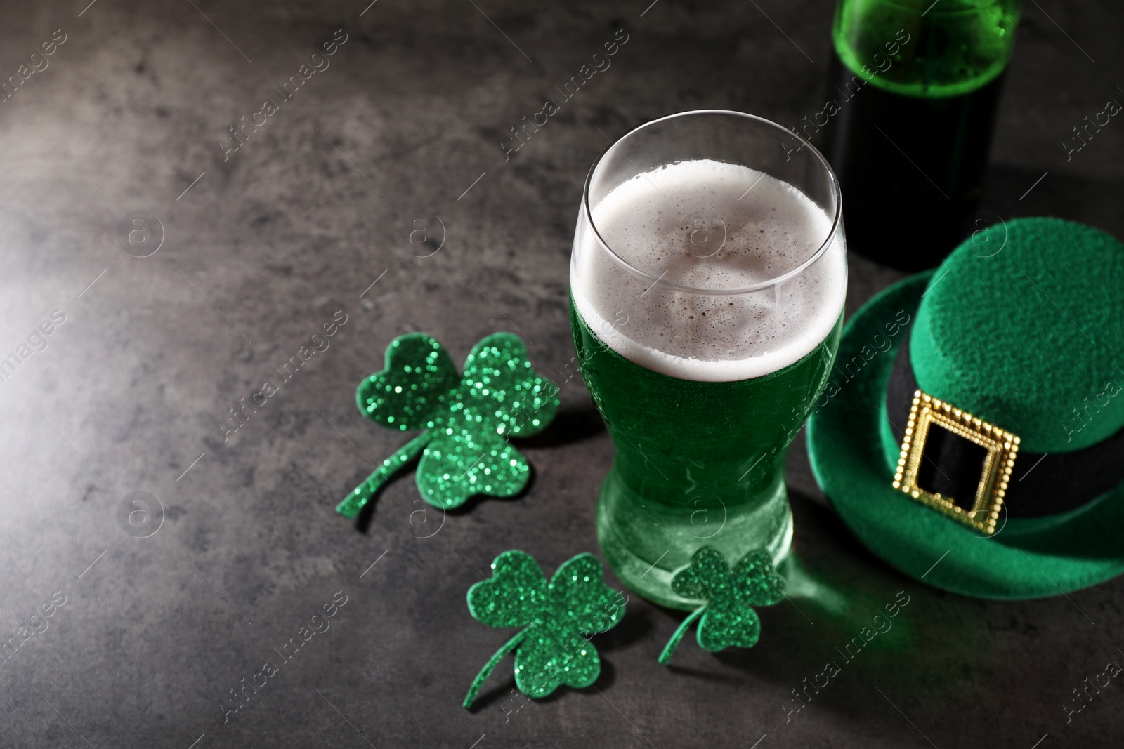 Photo of St. Patrick's day celebration. Green beer, leprechaun hat and decorative clover leaves on grey table. Space for text