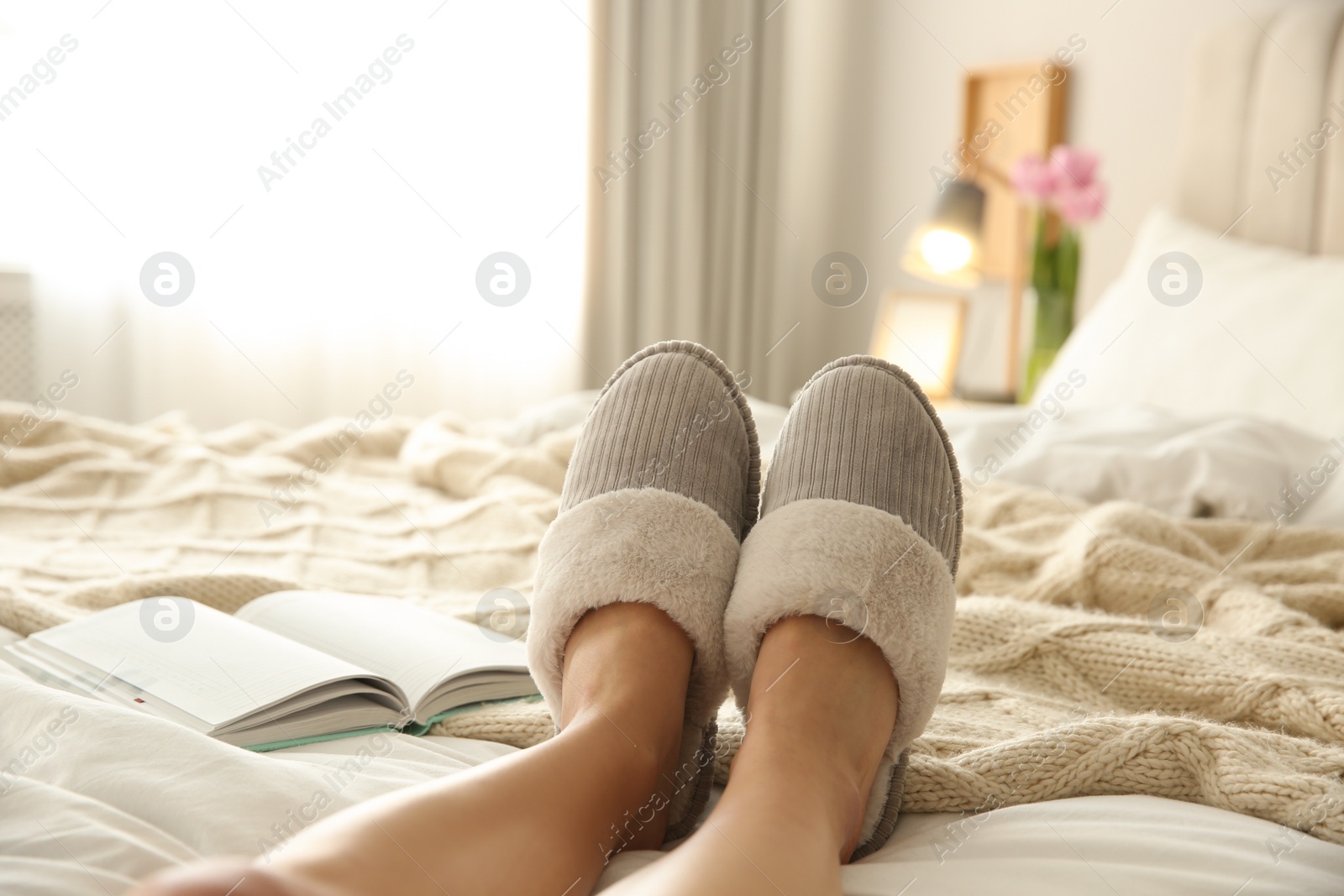 Photo of Woman wearing soft comfortable slippers on bed at home, closeup