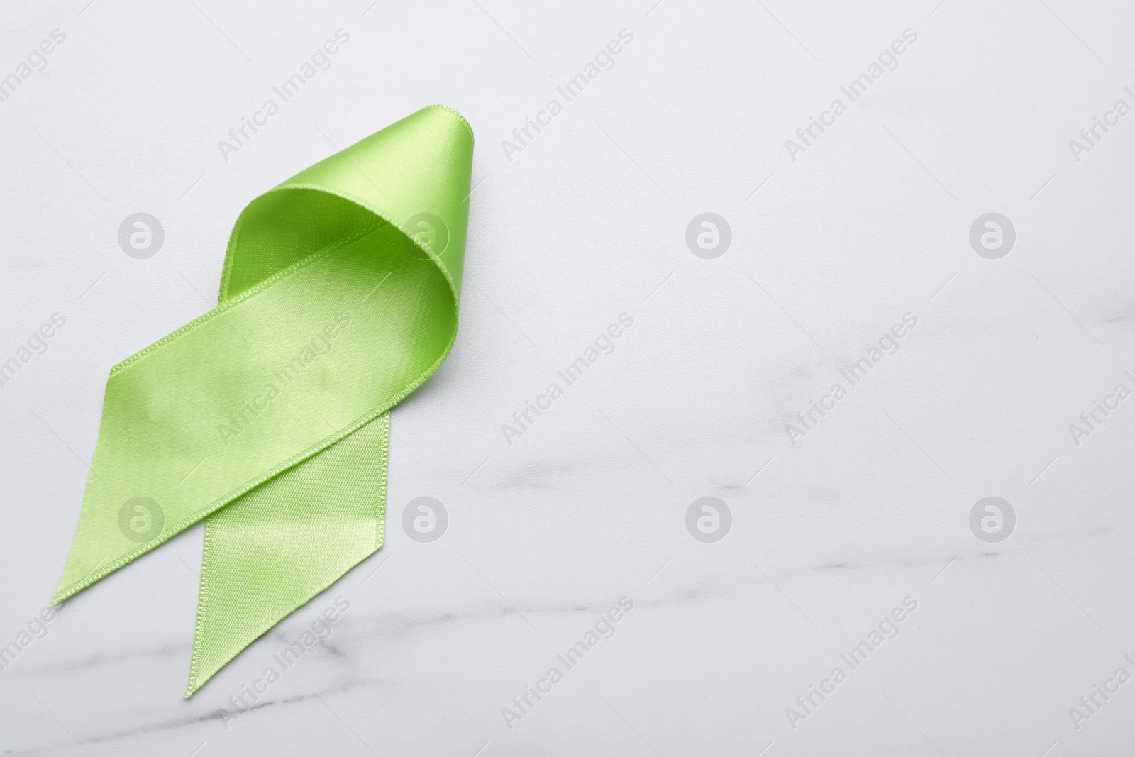 Photo of World Mental Health Day. Green ribbon on white marble table, top view with space for text